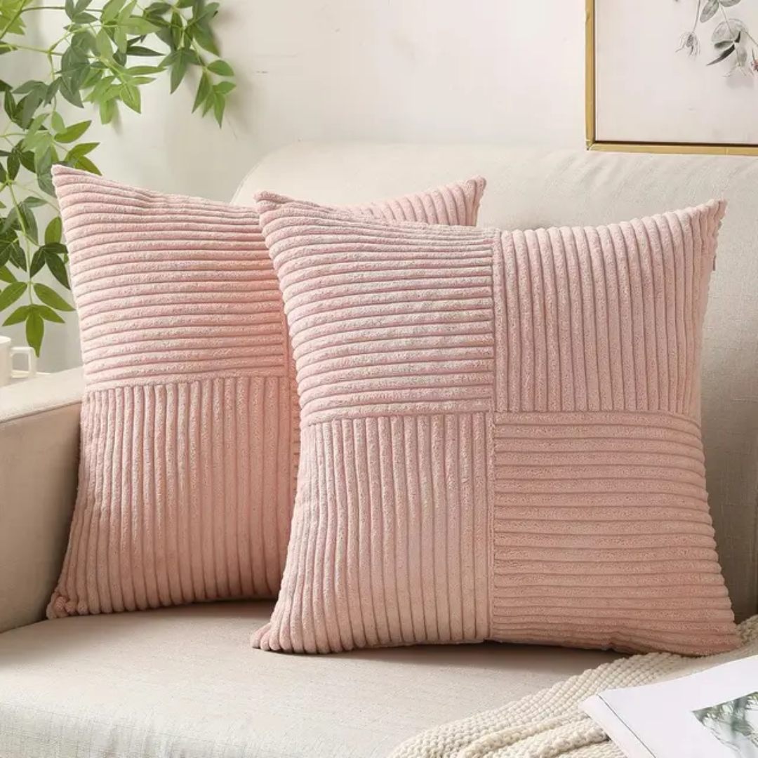 Two soft, dusty pink corduroy cushions with a checkered ribbed texture, displayed on a cream sofa in a bright room.
