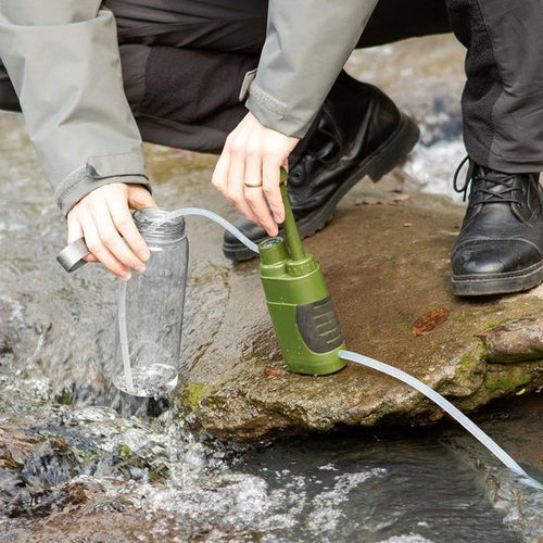 Green Fitlybuy portable survival water filter pumping water from a stream into a clear bottle.