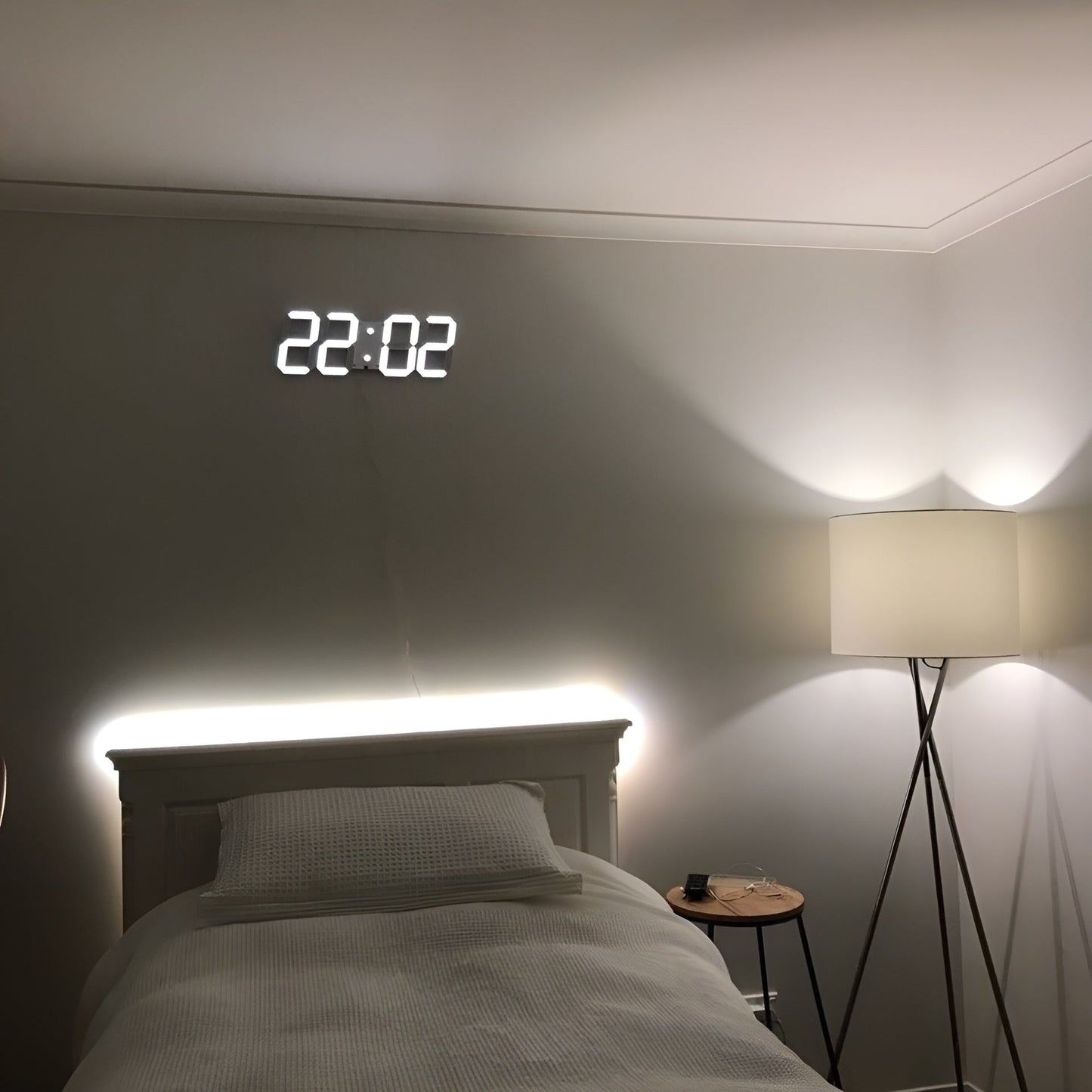 Fitlybuy PixelTime 3D LED digital wall clock showing time on a bedroom wall above a bed with a floor lamp nearby.