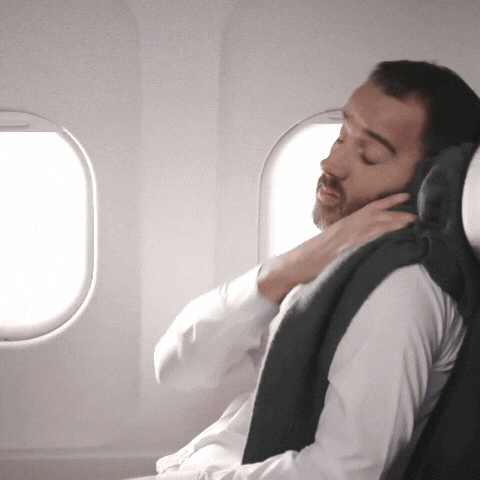 Man resting on an airplane using a grey Fitlybuy Butterfly ergonomic travel neck pillow for head and neck support.