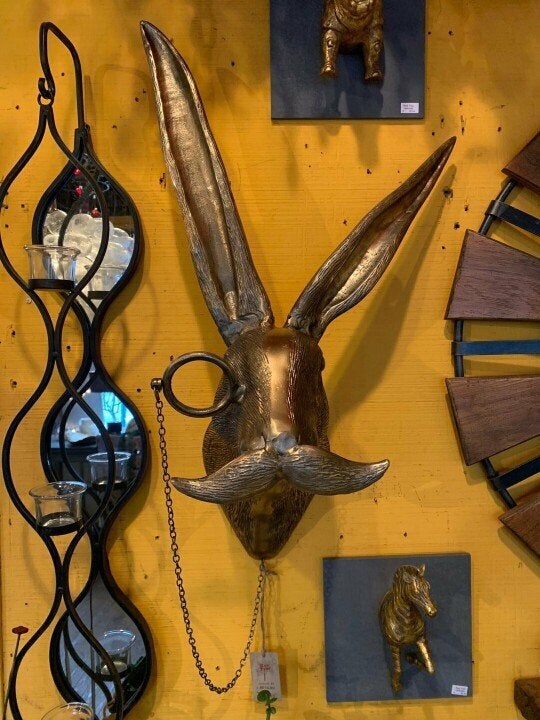 Bronze-colored rabbit head wall decor with a monocle and mustache, displayed on a yellow wall next to home accents.