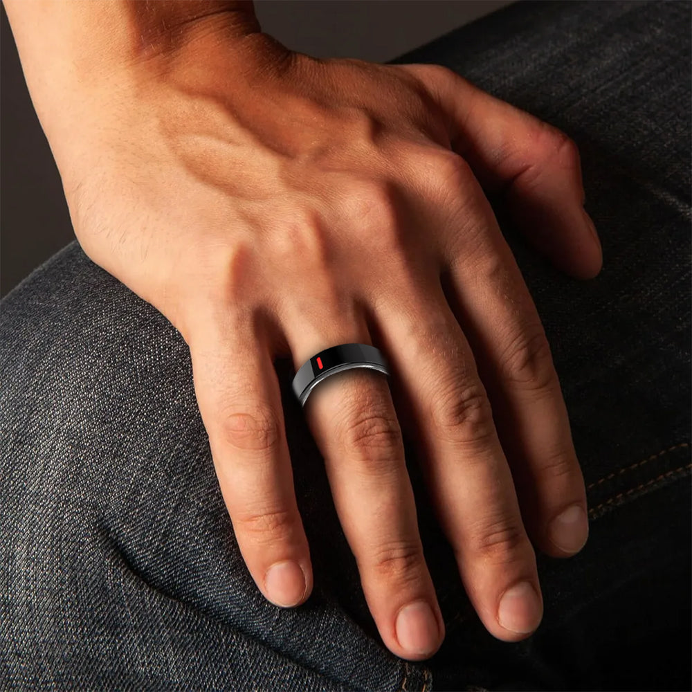 A black Fitlybuy Kexi-Life R03 smart ring with a red sensor light worn on a finger resting on blue denim jeans.