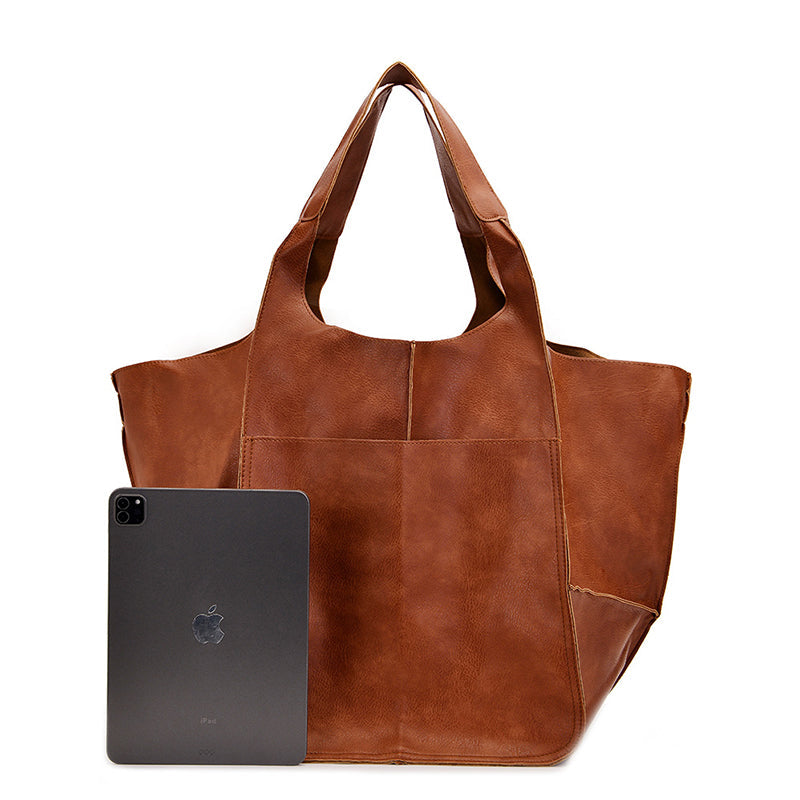 Fitlybuy oversized brown leather weekender tote with top handles and exterior pocket, shown next to a tablet for scale.
