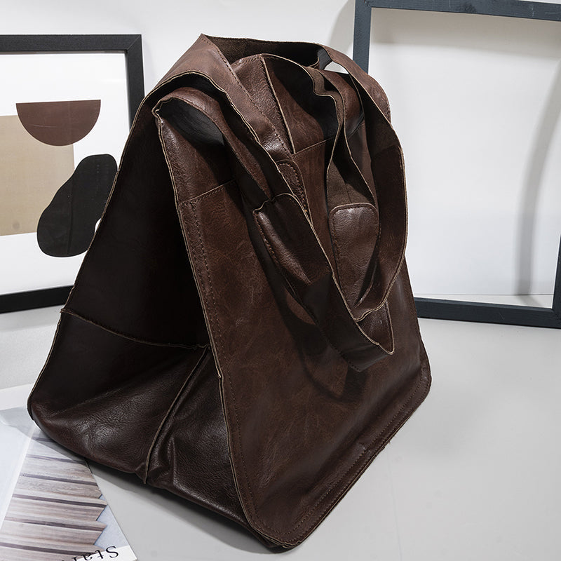 Fitlybuy oversized brown leather weekender bag with dual straps, shown on a table with modern framed wall art.