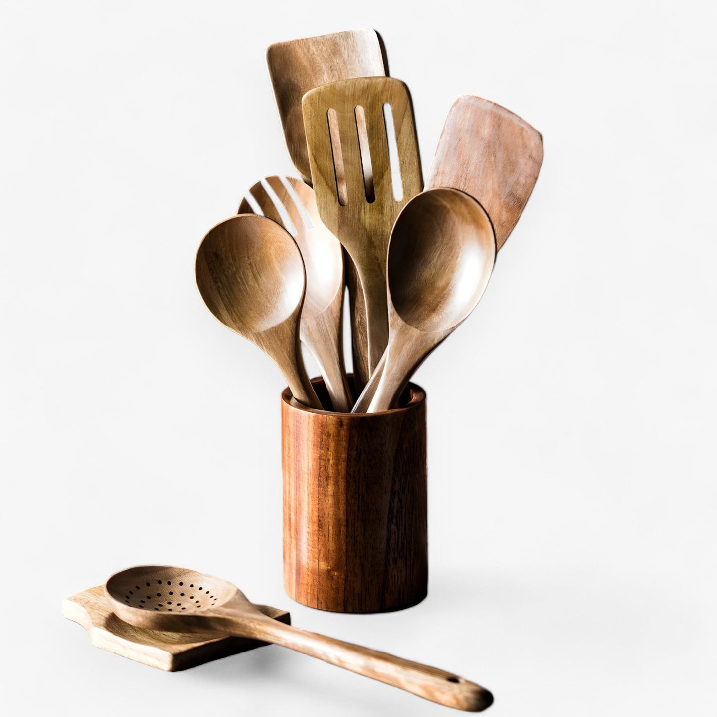 9-piece natural teak wood kitchen utensil set with a matching wooden holder and spoon rest, isolated on white.