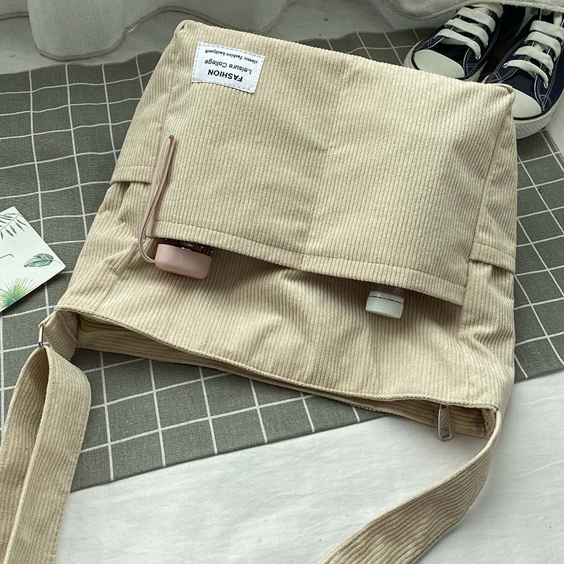 Beige corduroy Fitlybuy crossbody bag with front pockets, "Fashion" label, and wide strap on a grid surface.