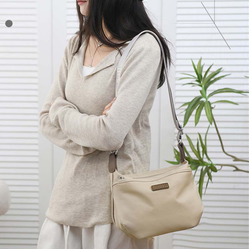 A woman wearing a beige Fitlybuy Joanna anti-theft waterproof crossbody shoulder bag with a secure zipper design.