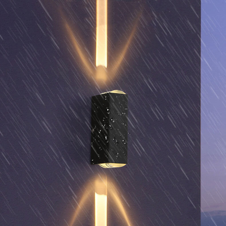 Waterproof black rectangular LED outdoor wall light emitting upward and downward beams on a wet exterior wall.