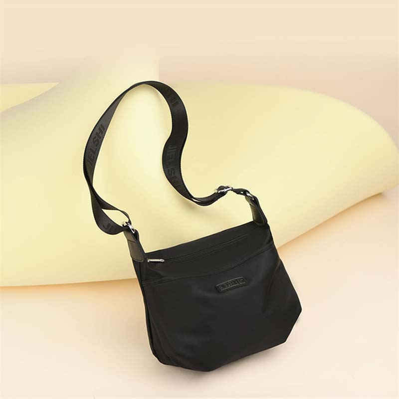 Fitlybuy Joanna black waterproof anti-theft crossbody bag with an adjustable branded shoulder strap on a yellow backdrop.