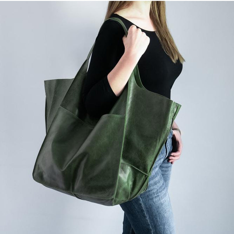 Woman wearing an oversized, forest green leather weekender bag on her shoulder for stylish travel.