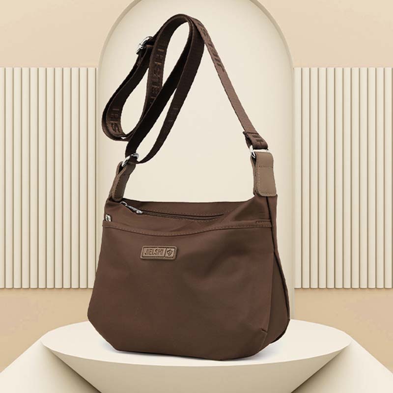Brown Fitlybuy anti-theft waterproof crossbody bag with adjustable strap and front zip pocket, displayed on a pedestal.