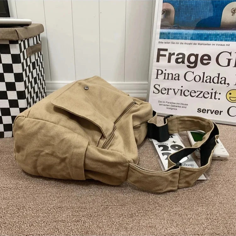 Tan canvas Fitlybuy CrossStream sling bag with a flap closure, zip pocket, and adjustable shoulder strap on a carpet.