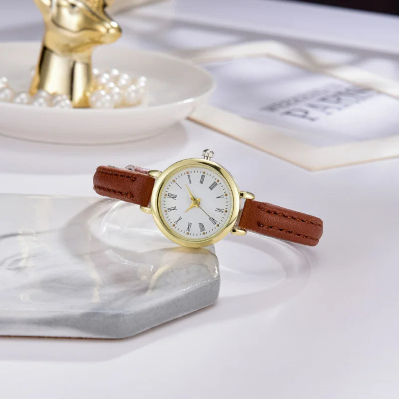 Fitlybuy Billie gold minimalist women's watch with white dial, Roman numerals, and brown leather strap on marble base.