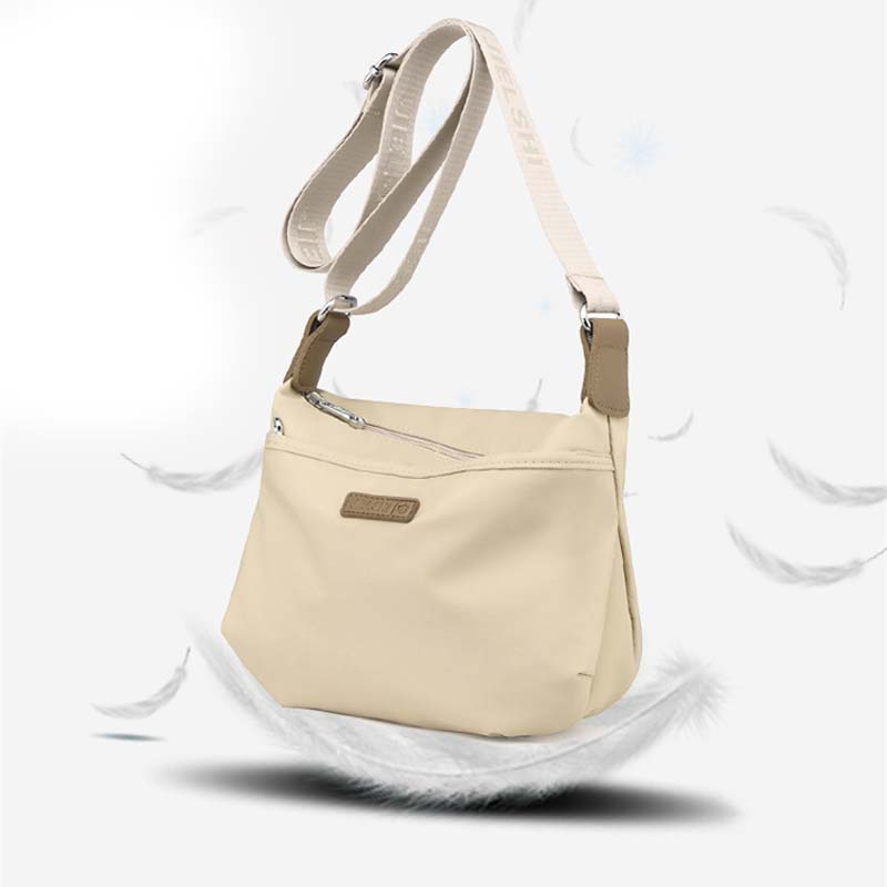 Beige Fitlybuy Joanna waterproof crossbody bag with adjustable strap and zip closure, surrounded by floating feathers.