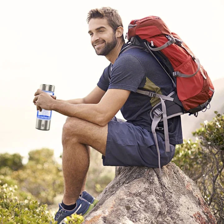 Hiker sitting on a rock holding a Fitlybuy silver and blue glowing hydrogen generator water bottle.
