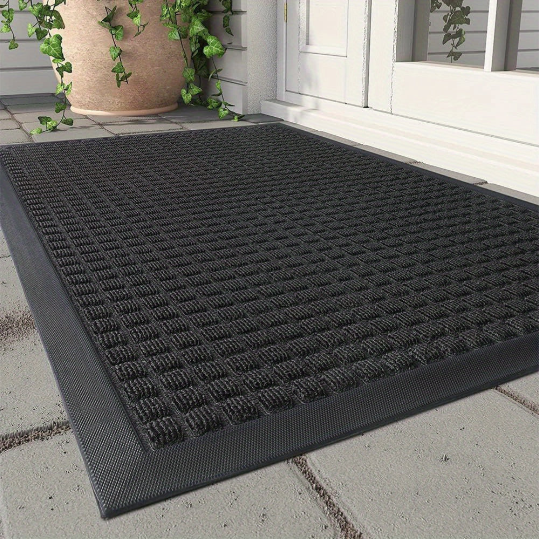Dark grey, rectangular indoor/outdoor door mat with a textured dirt-trapping grid pattern placed at a home entrance.