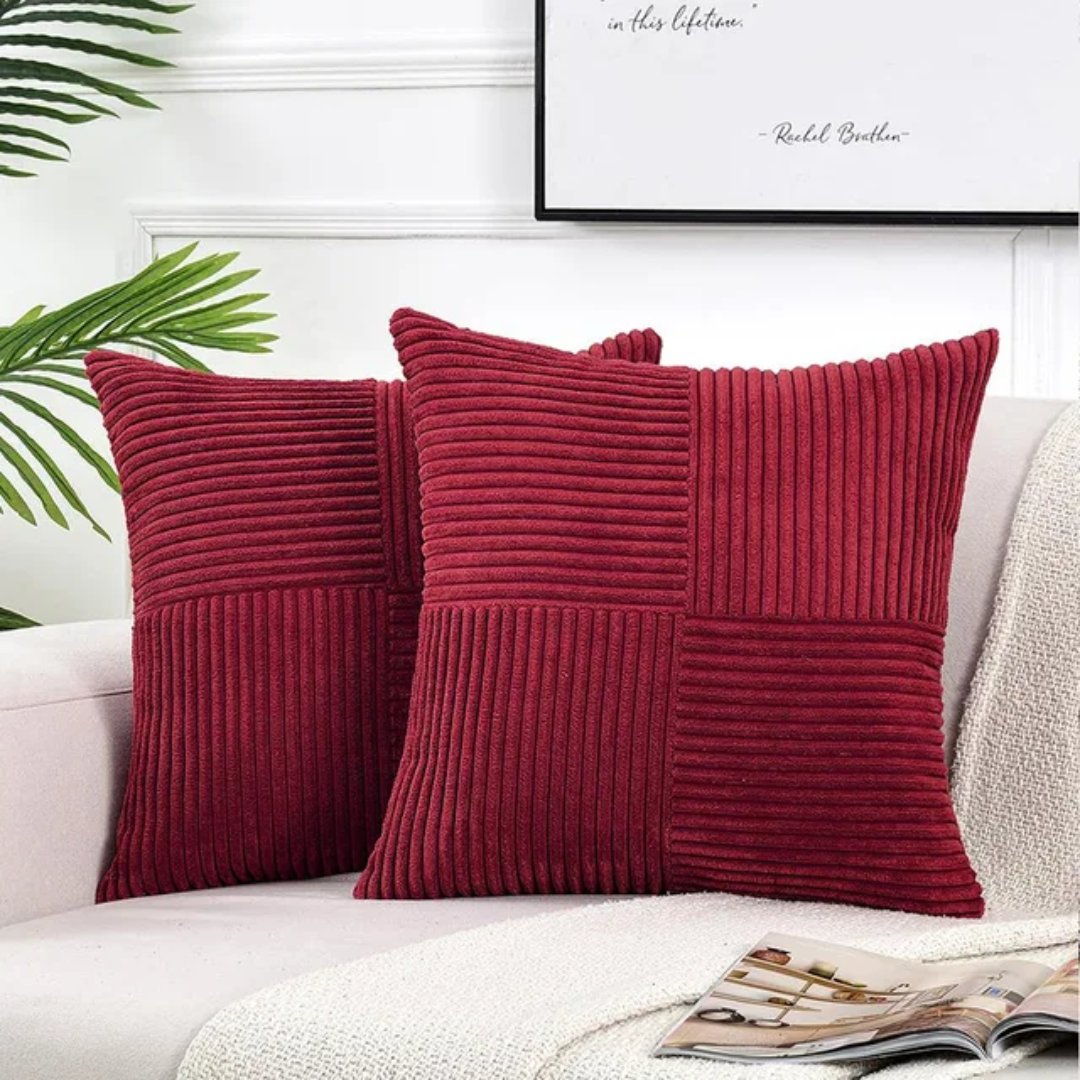 Two deep red, corduroy-textured square cushions on a beige sofa, featuring a modern paneled design.