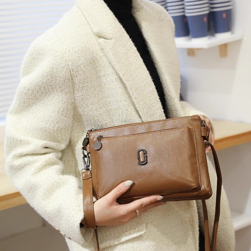 Fitlybuy Fosh small brown leather shoulder bag with a rectangular metal clasp, held by a woman in a cream blazer.