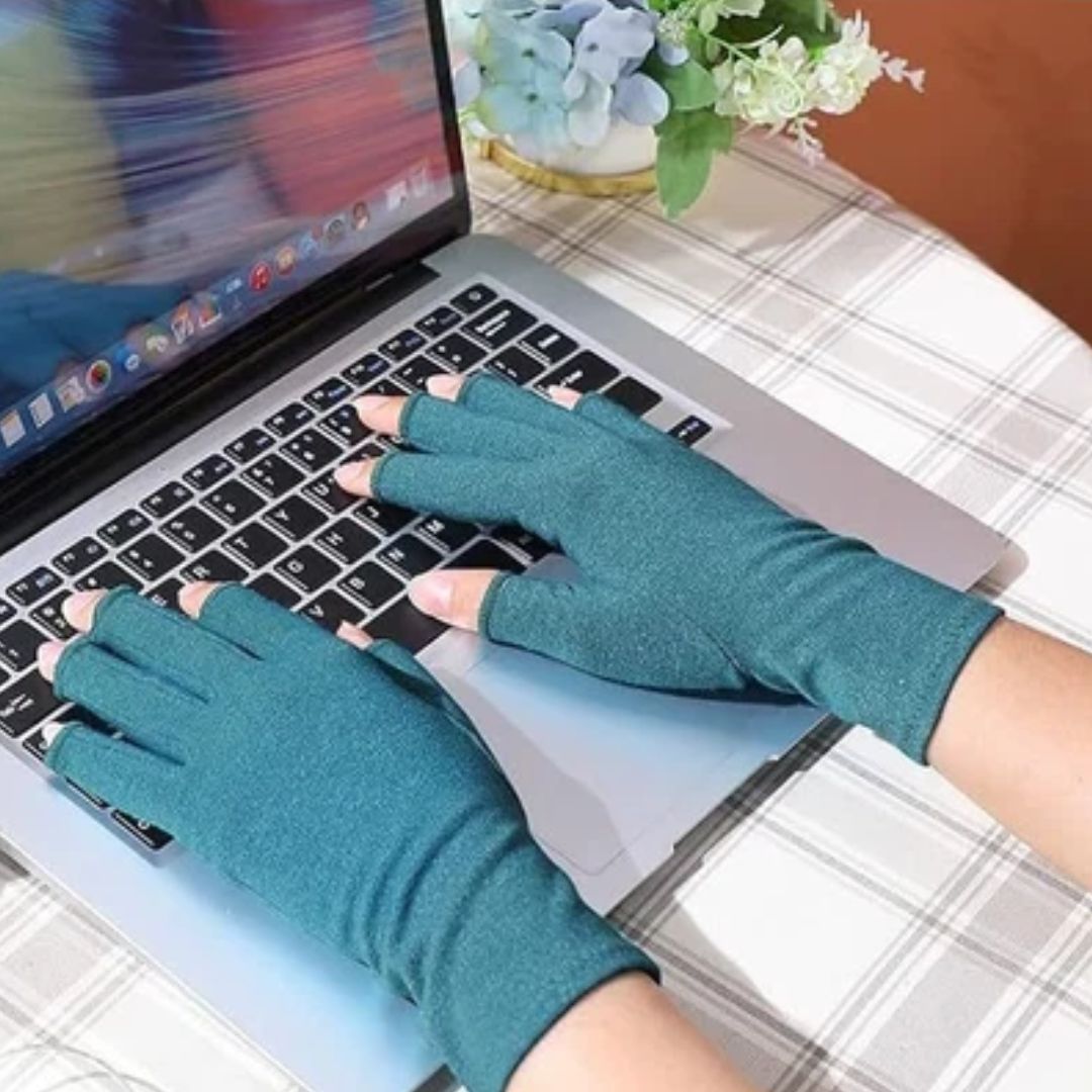 Person wearing dark green, fingerless Fitlybuy therapeutic heat gloves while typing on a laptop at a table.