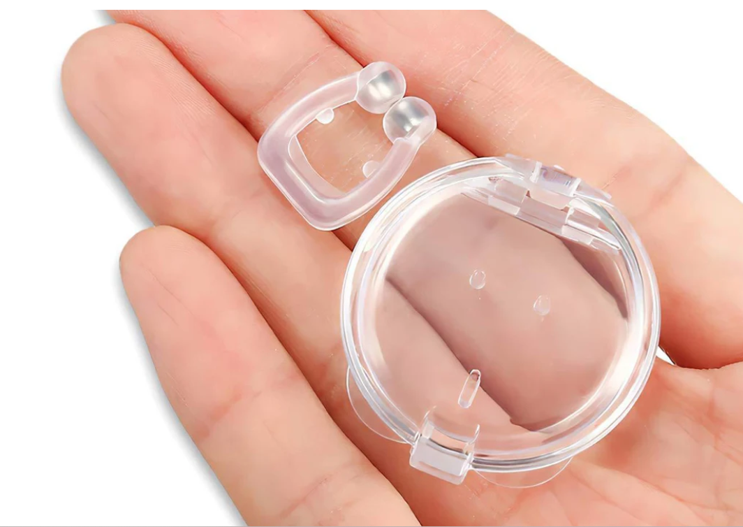 Clear Fitlybuy anti-snoring magnetic nose clip and round travel case held in a person's palm.