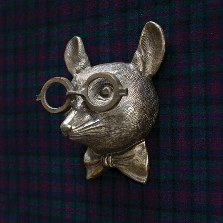 Silver-toned animal head wall decor wearing glasses and a bow tie, mounted on a dark green plaid fabric background.