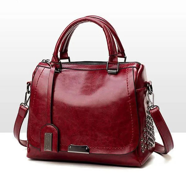 Elegant dark red soft leather shoulder bag with a top handle, detachable strap, and metallic stud side detailing.