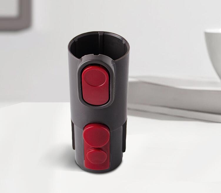 Fitlybuy DogCatFri grey vacuum brush attachment with red release buttons, shown against a blurred indoor tabletop.
