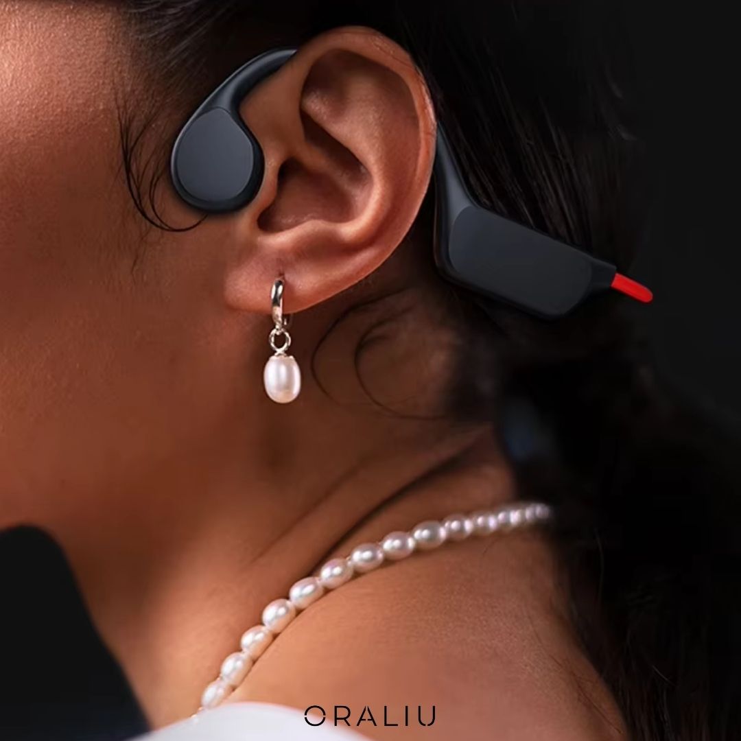 Close-up of black Fitlybuy bone conduction headphones on a person wearing a pearl necklace and earrings.