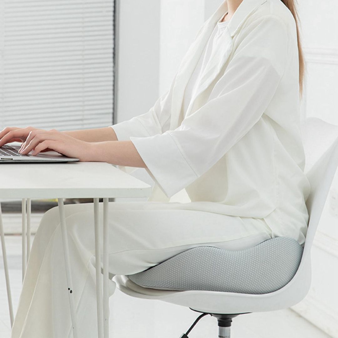 Person sitting on an ergonomic gray Fitlybuy sciatica relief cushion on a white office chair.
