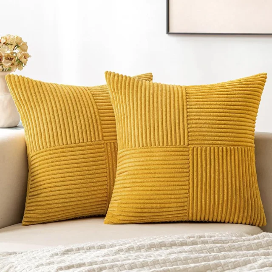 Two mustard yellow corduroy throw pillows with a textured, square-blocked pattern resting on a white sofa.