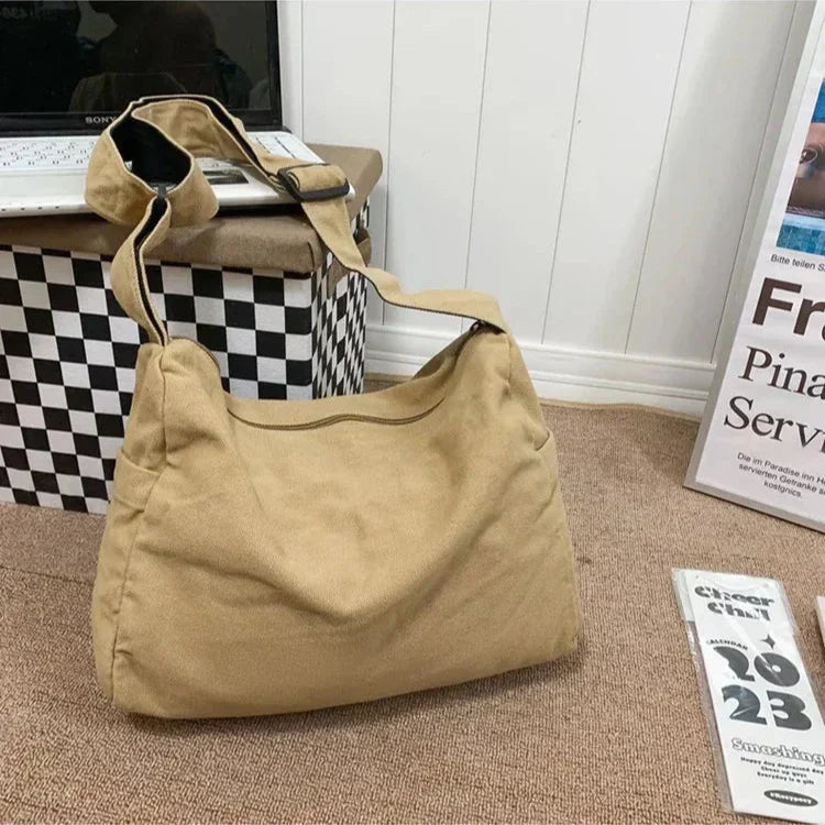 Tan canvas CrossStream messenger bag with an adjustable shoulder strap, resting on a textured surface.
