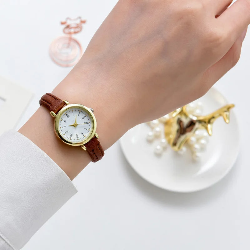 Fitlybuy Billie gold round watch with white dial, Roman numerals, and brown leather strap worn on a woman's wrist.