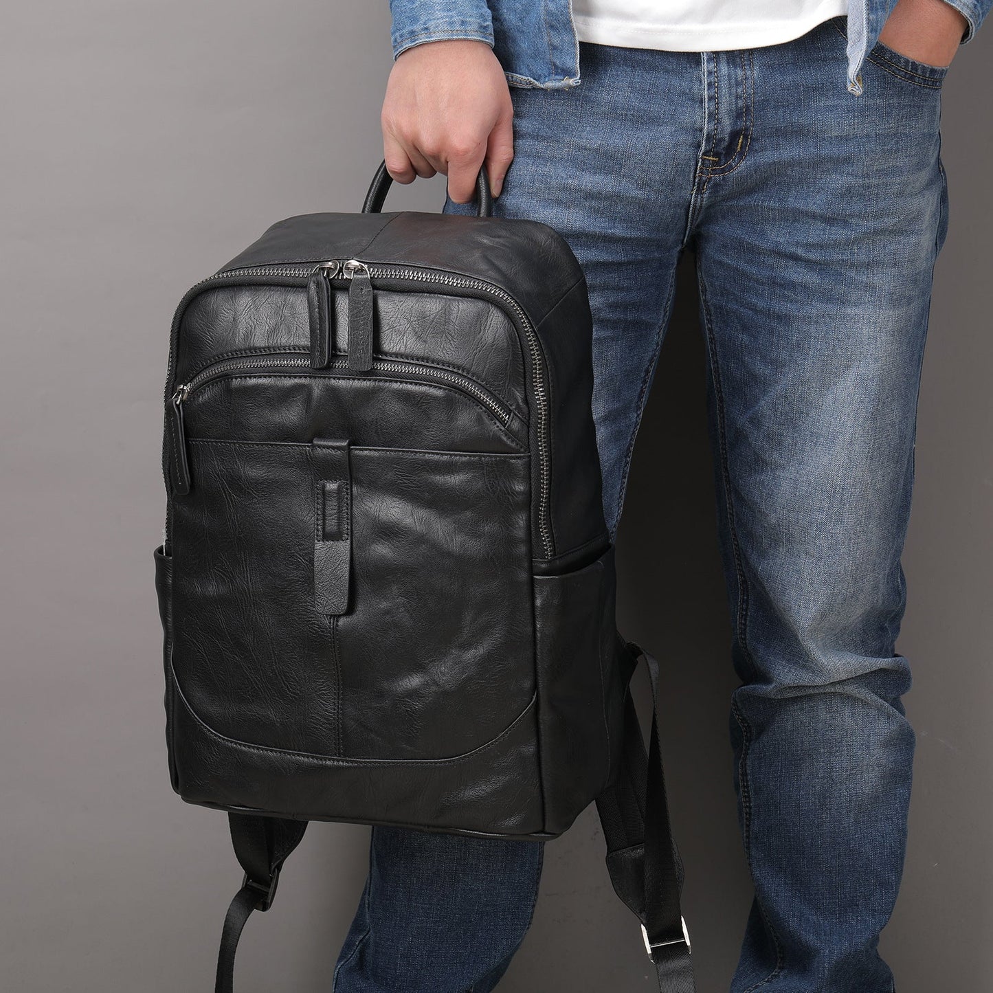 Fitlybuy Prestige Voyager black leather laptop backpack with multiple zippered pockets, held by a person in blue jeans.