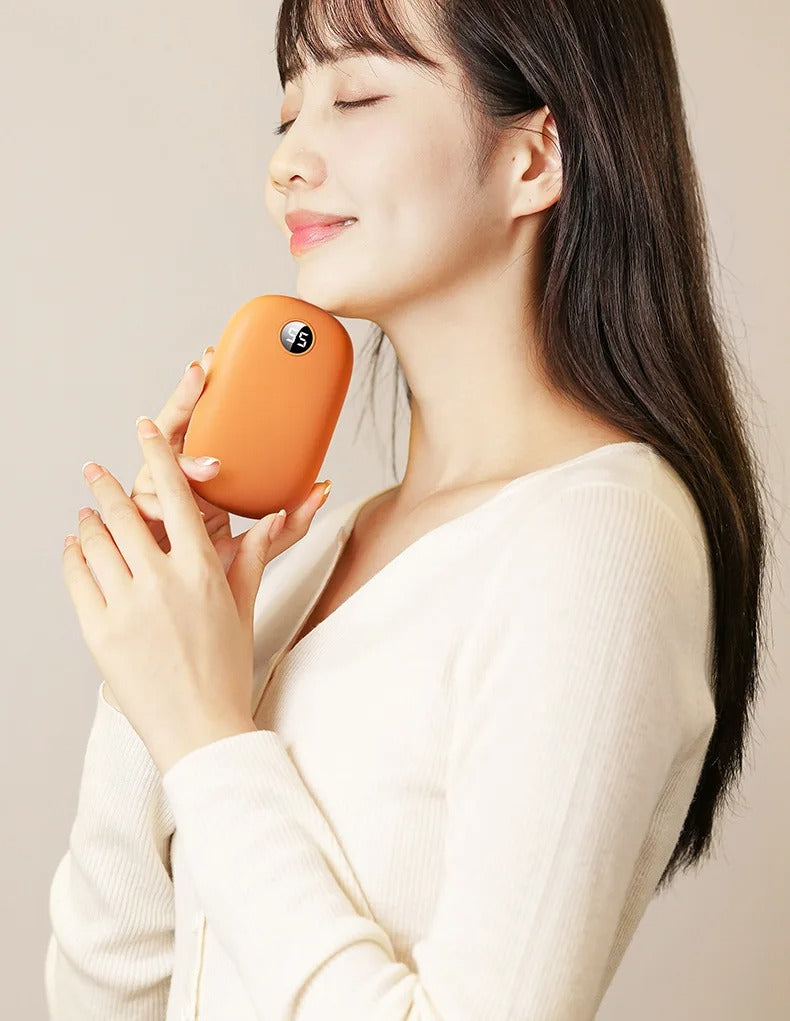 Woman holding an orange Fitlybuy 2-in-1 hand warmer and power bank with digital display near her face.