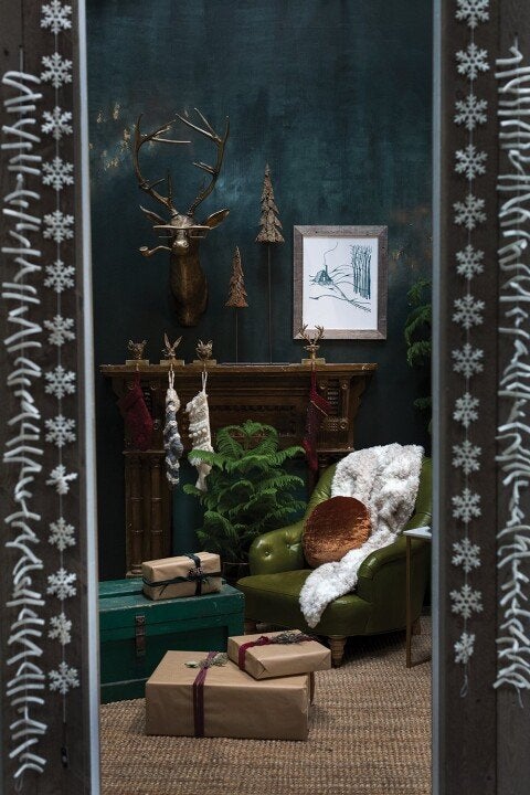 Gold deer head wall decor with glasses and pipe, displayed above a fireplace in a festive, cozy holiday living room.