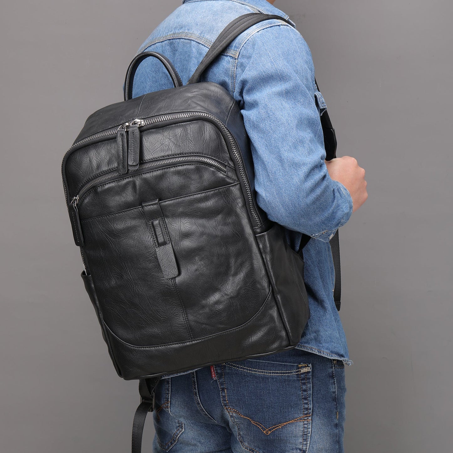 Person wearing a black leather Fitlybuy Prestige Voyager laptop backpack with multiple zippered pockets and sturdy straps.