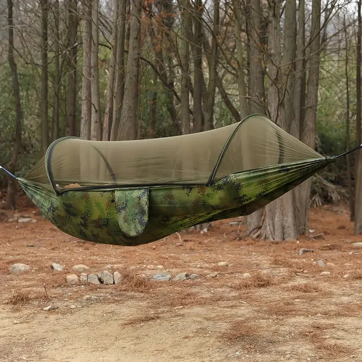 Fitlybuy camouflage camping hammock with integrated BugShield mosquito net hanging between trees in a forest.