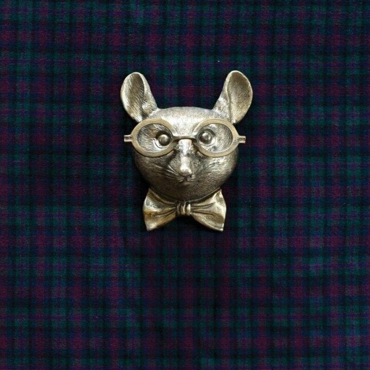 Antique brass-tone mouse wall decor wearing glasses and a bowtie, centered against a dark green plaid fabric background.