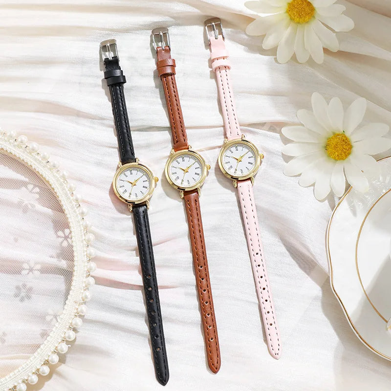 Three Fitlybuy Billie gold watches with Roman numerals on black, brown, and pink straps, displayed on white fabric.