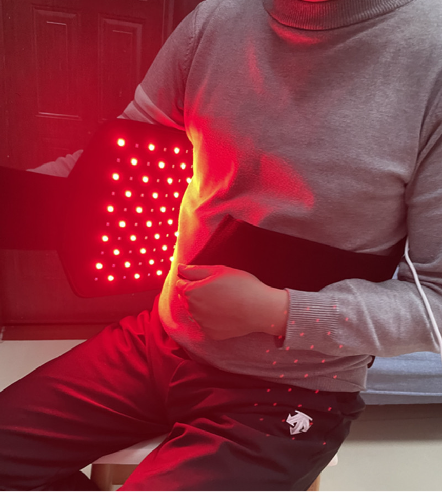 Person wearing a black Fitlybuy red light therapy belt with glowing infrared LEDs for slimming and relaxation.