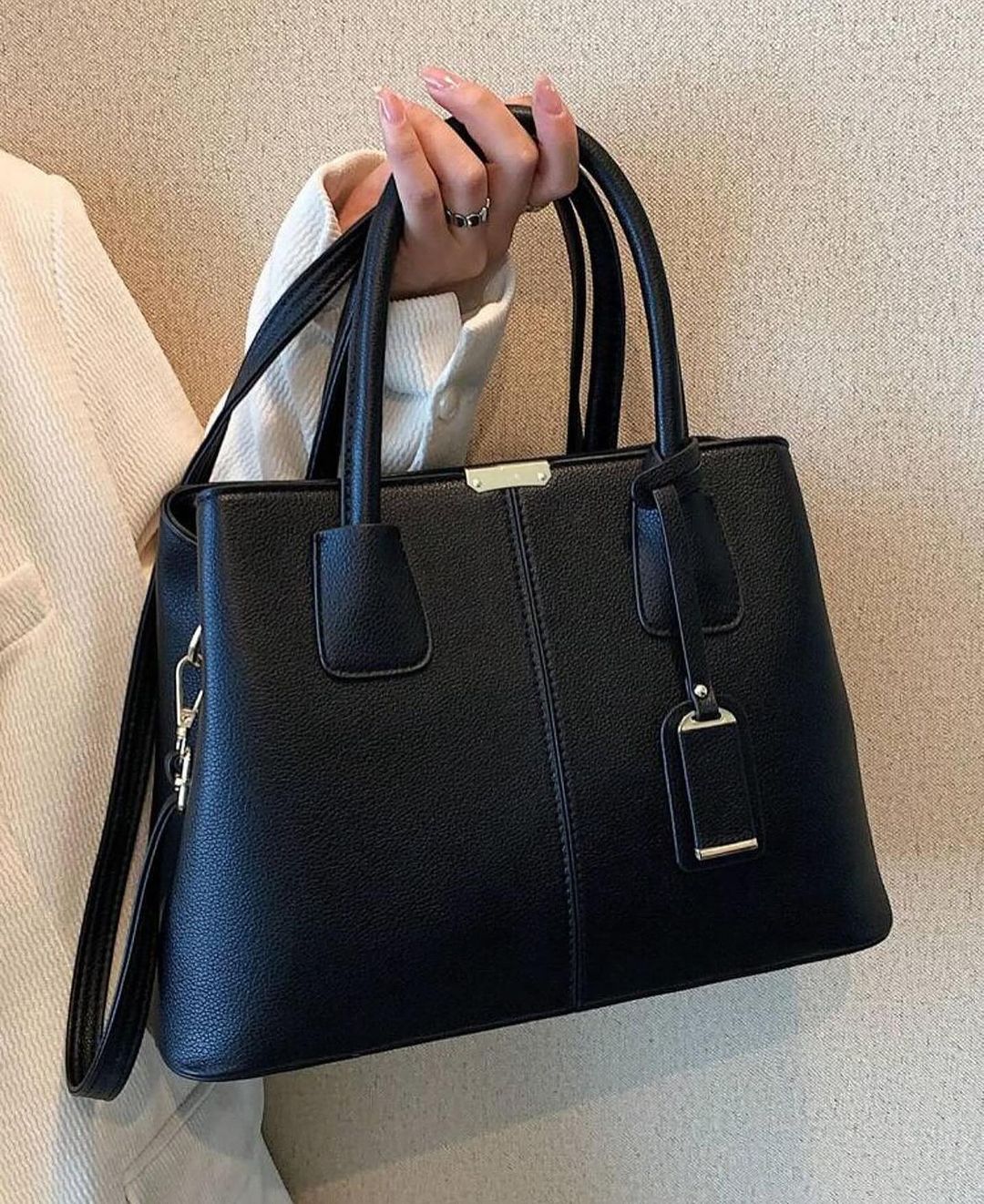 Black Fitlybuy PU leather handbag with dual handles, detachable strap, and gold-tone hardware, held by a hand.