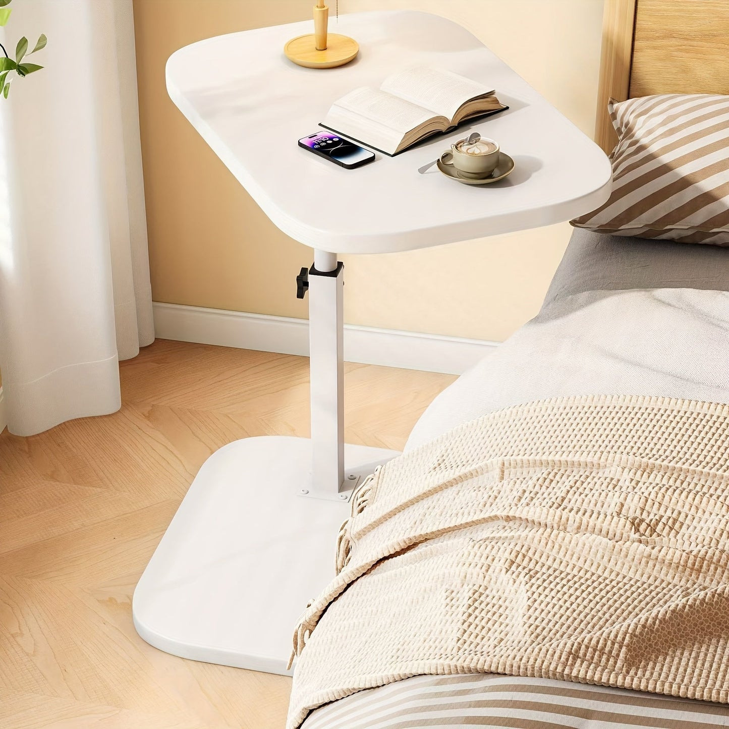 Fitlybuy white adjustable side table with a C-shaped base beside a bed, holding a book, phone, and cup of coffee.