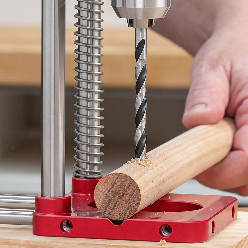 Fitlybuy red metal precision woodworking locator drilling a hole into a wooden dowel rod on a workshop table.
