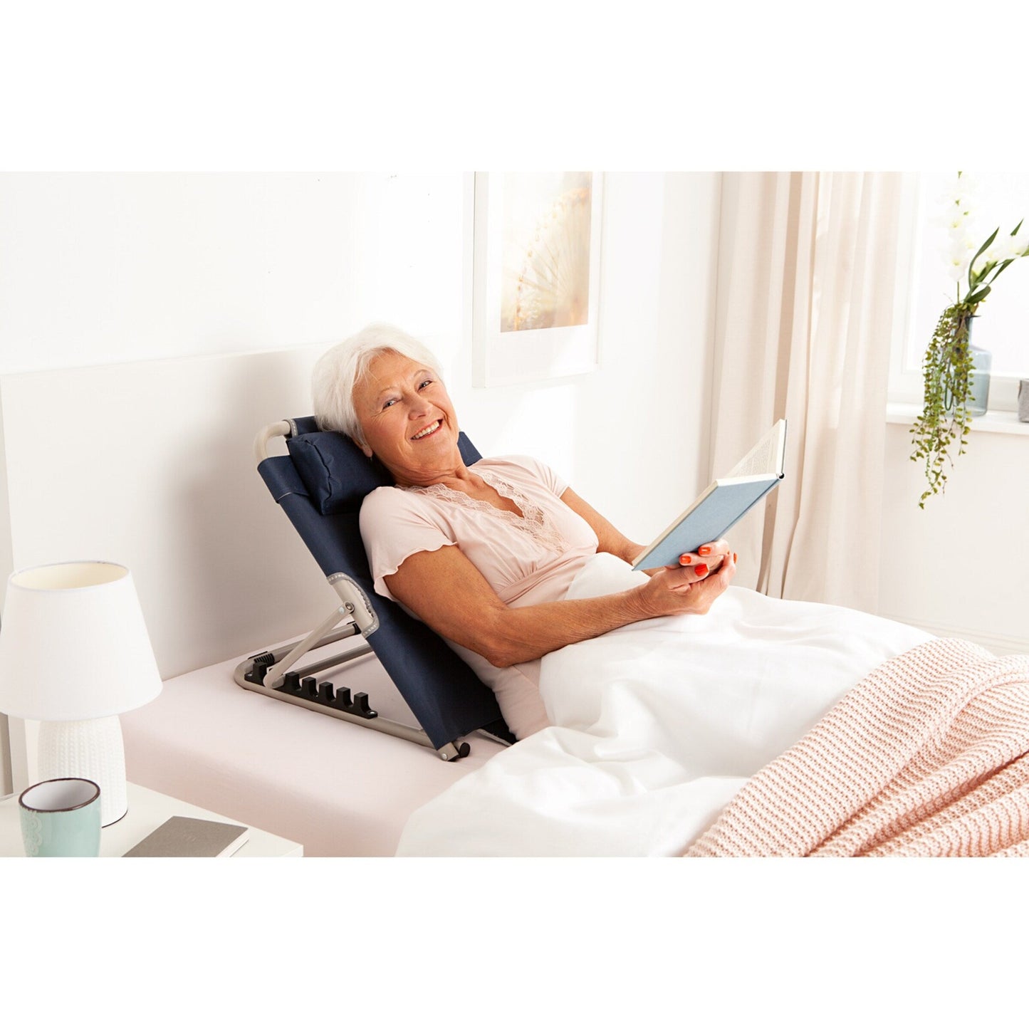 Senior woman reads in bed using a navy blue Fitlybuy LumbarLux adjustable backrest with a removable head cushion.
