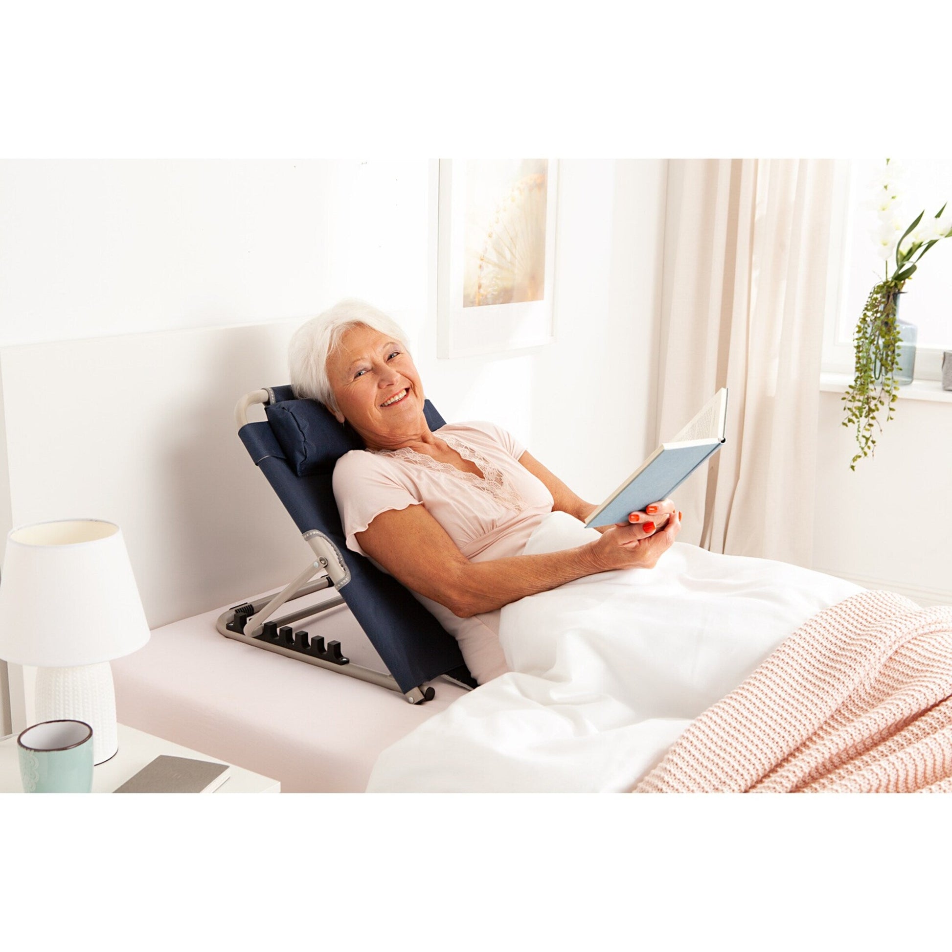 Senior woman reads in bed using a navy blue Fitlybuy LumbarLux adjustable backrest with a removable head cushion.