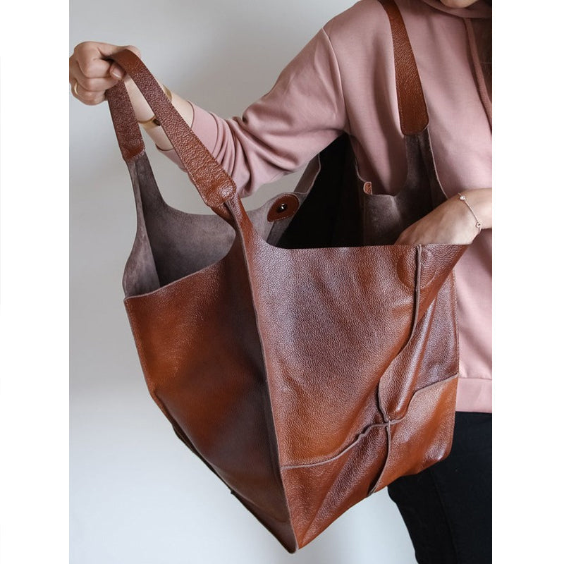 Person holding a large, brown, pebbled leather Fitlybuy oversized weekender tote bag with wide shoulder straps.
