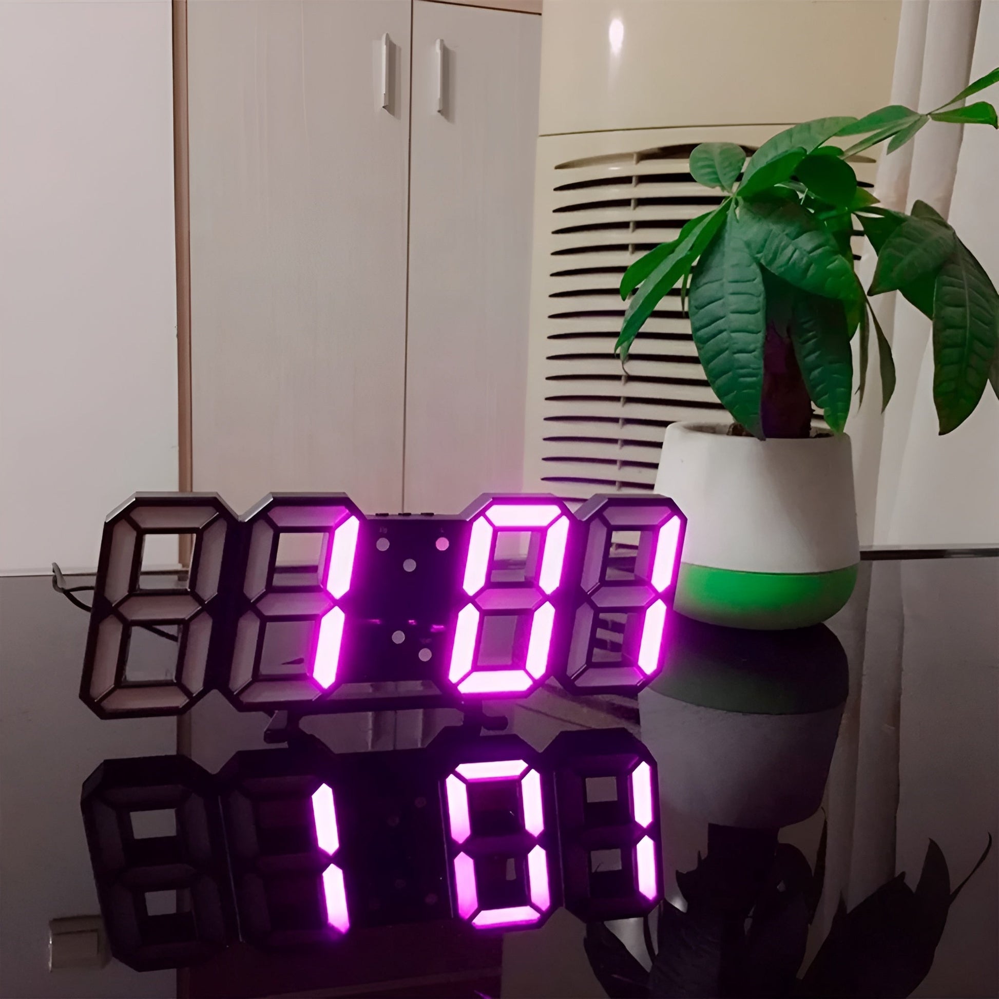 Fitlybuy 3D LED digital wall clock with pink glowing digits, showing time on a reflective desk near a houseplant.