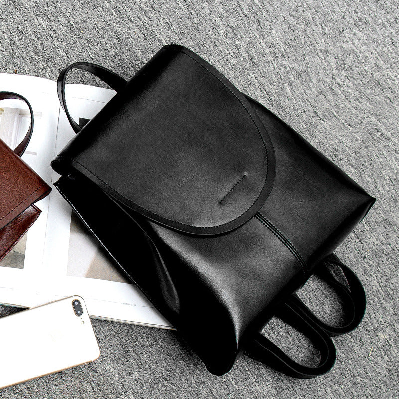 Fitlybuy black leather backpack with a flap closure, sitting on an open magazine next to a smartphone.