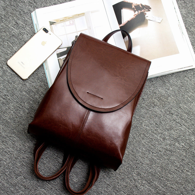 Fitlybuy brown leather backpack with rounded flap, top handle, and adjustable straps on a gray background with a phone.