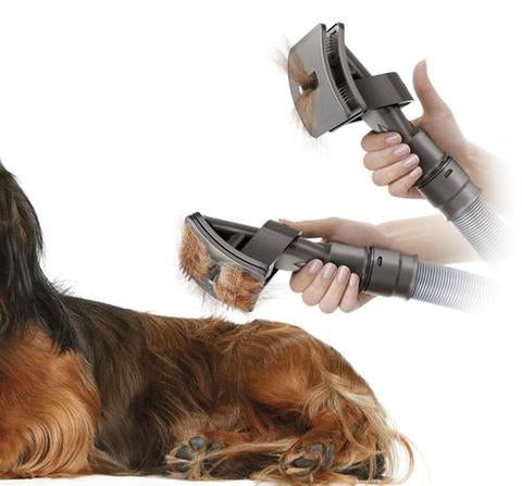 Fitlybuy grey vacuum grooming brush removing hair from a brown dog, demonstrating the self-cleaning hair release feature.
